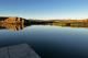 A calm lake reflects the nearby cliff.